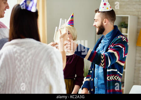 Groupe de professionnels jeunes gens portant des chapeaux de fête anniversaire avec friends clinking champagne verres pendant party at home Banque D'Images