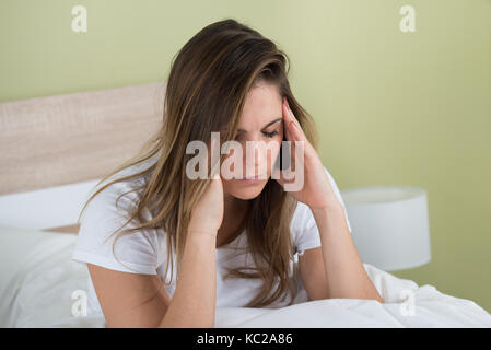 Portrait d'une jeune femme avec des maux de sitting on bed Banque D'Images