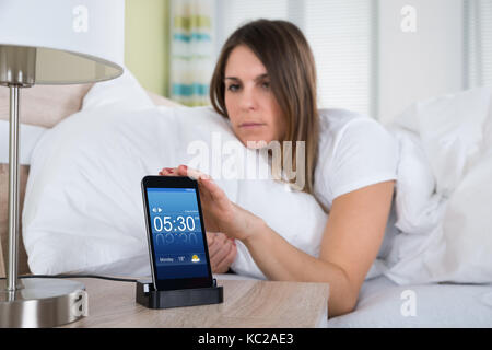 Young woman lying on bed snoozing alarme sur téléphone mobile Banque D'Images