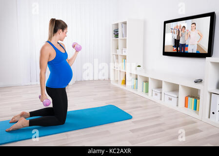 Femme enceinte faire de l'exercice avec haltères sur le tapis à la maison Banque D'Images