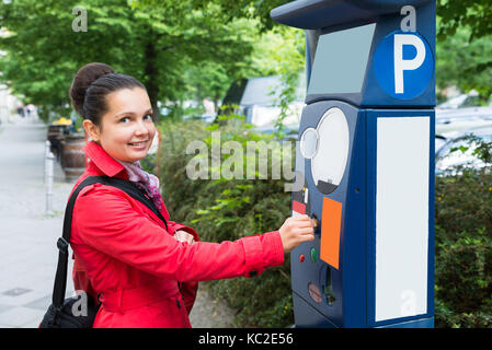 Jeune femme belle l'insertion d'une pièce de monnaie pour Parking Meter Banque D'Images