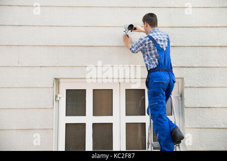 Homme technicien sur l'escabeau installation de caméra de surveillance sur le mur Banque D'Images