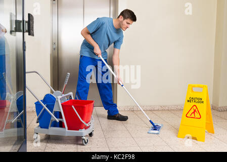 Heureux homme janitor avec équipements de nettoyage nettoyage à l'étage Banque D'Images