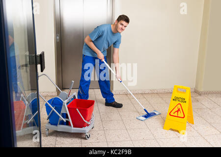 Heureux homme janitor avec équipements de nettoyage nettoyage à l'étage Banque D'Images