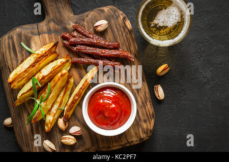 Des collations variées pour la bière. Pommes de terre rissolées pepperoni les noix et un verre de bière. Banque D'Images