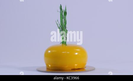 Gâteau de mousse jaune contemporain décoré de caramel vert, sur fond blanc Banque D'Images