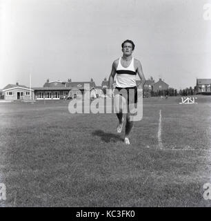Années 1960, historique, l'image montre un athlète masculin de porter une veste et pantalon de s'entraîner seul à l'extérieur dans un champ d'herbe, Englad, UK. Banque D'Images