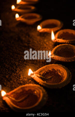 Happy diwali - nombreux diya en terre cuite ou lampes à huile disposées sur surface de l'argile ou la masse dans une ligne ou courbe ou forme de zigzag, selective focus Banque D'Images