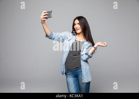 Temps selfies. attractive young woman in casual wear décisions par son selfies téléphone intelligent et souriant tout en se tenant à l'arrière-plan gris Banque D'Images