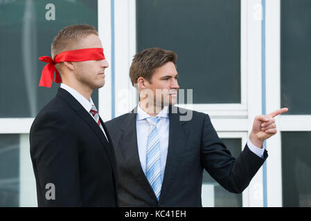 Certain jeune homme d'aider les partenaires à l'extérieur du bureau, les yeux bandés Banque D'Images