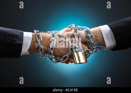 Gros plan du enchaîné businessmen shaking hands against blue background Banque D'Images