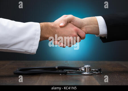 Portrait of woman doctor shaking hands with stethoscope on table Banque D'Images