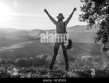 Découvrir une vue magique de la toscane. vu de dos femme sac Randonneur admirant le coucher du soleil avec en Toscane et de réjouissance Banque D'Images