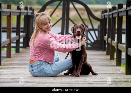 Blonde girl smiling with dog labrador.labrador assis à côté Banque D'Images