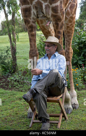 Le port touristique hat pose assis sur une chaise en face d'eric une personne-friendly girafe à elsamere kenya naivasha Banque D'Images