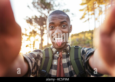 Jeune homme africain faisant des grimaces et en tenant vos autoportraits en plein air Banque D'Images