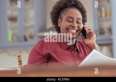 Smiling african woman reading paperwork et parler sur son portable Banque D'Images