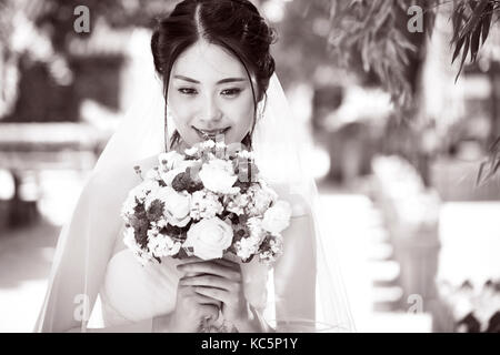 Belle et heureuse jeune Asian bride wearing wedding dress holding a bouquet de fleur, noir et blanc. Banque D'Images