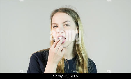 Charmante jeune femme souriante met en bouche un chewing-gum sur fond blanc Banque D'Images