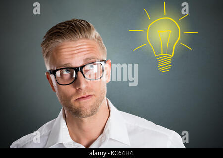Jeune homme intelligent avec expression réfléchie avec l'idée de l'ampoule sur fond gris Banque D'Images