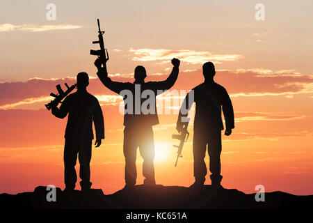 Silhouette de soldats avec des fusils contre ciel dramatique