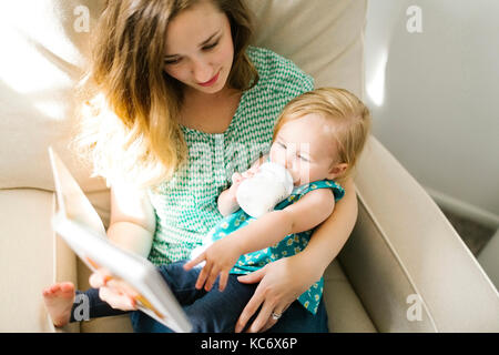 Mother with baby girl (12-17 mois) assis dans la salle de séjour et reading book Banque D'Images