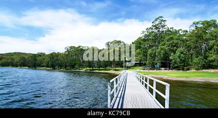 Paysage au bord de l'eau avec une jetée, ciel bleu, nuage blanc et un arbre constellé horizon sur l'eau. lake Macquarie, côte centrale de la Nouvelle-Galles du Sud. Banque D'Images