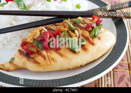 Calamars grillés, marinés dans la sauce de soja, de gingembre et de piment sur une plaque blanche avec du riz cuit. la cuisine orientale. Banque D'Images