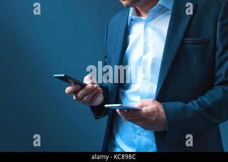 Synchroniser et sauvegarder les données sur deux téléphones mobiles, l'homme en costume d'affaires synchronise des fichiers, messages et informations de contact sur smartphone privés et d'entreprises Banque D'Images