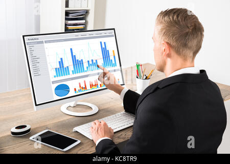 Jeune homme d'analyser les graphiques sur ordinateur à l'office de tourisme Banque D'Images