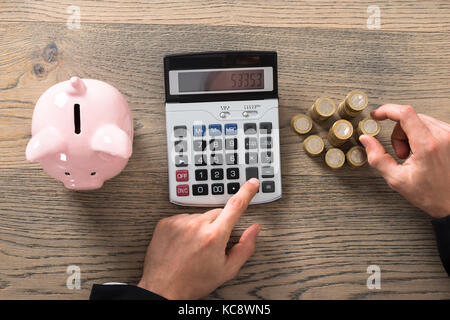 Close-up of a businessman à compter des pièces en utilisant calculator at desk in office Banque D'Images
