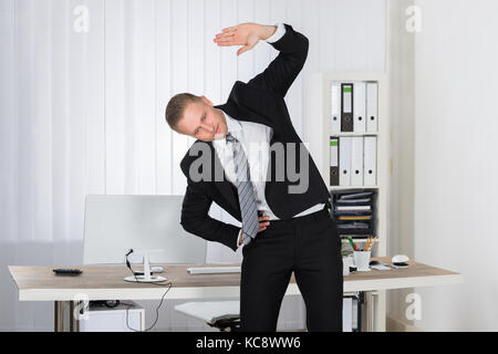 Portrait of a young businessman stretching in office Banque D'Images