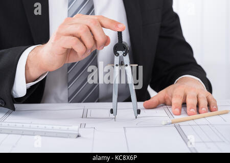 Close-up of young male hands holding compass sur blueprint at desk in office Banque D'Images