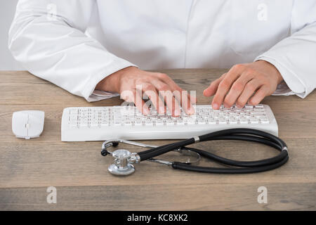 Close-up of male doctor de la saisie sur clavier d'ordinateur avec la souris au bureau en bois en clinique Banque D'Images