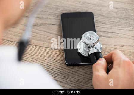 Close-up of doctor holding stethoscope on smart phone au bureau en bois en clinique Banque D'Images