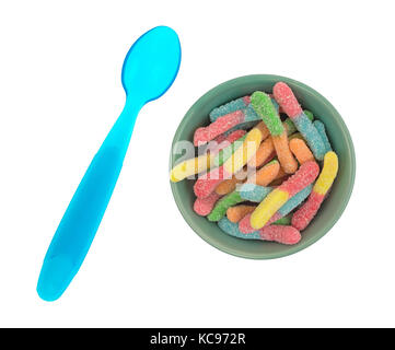 Vue de dessus d'une portion de sucre coloré dégustation aigre couché gummy worms dans un bol de petit-déjeuner avec une cuillère en plastique bleu sur le côté isolé sur fond blanc Banque D'Images
