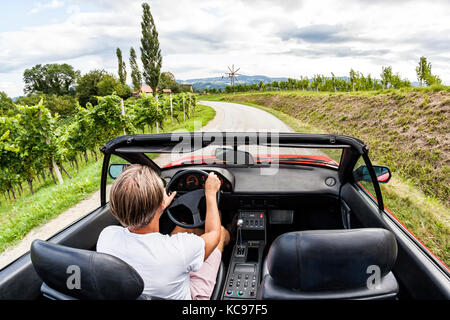 Jeune homme roulant avec voiture de sport vintage rouge à travers le vignoble sur vigne du sud de la Styrie en Autriche. route moulin appelé klapotetz en face. Banque D'Images
