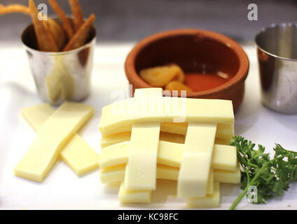 Fromage Cheddar coupé en lamelles sur une plaque blanche. Les croustilles de maïs dans une coupe d'argent et les abricots séchés avec une cuvette d'argile Banque D'Images