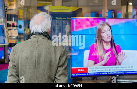 Homme chauve plus âgé avec le dos tourné regardant une télévision exposée dans un magasin Banque D'Images