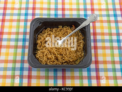 Une portion de nouilles ramen saveur de boeuf avec une fourchette dans un bac allant au noir sur un tapis coloré. Banque D'Images