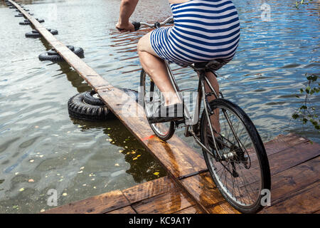 Festival tchèque, Un cycliste sur une passerelle en bois tente de traverser l'étang, un vélo de sport inhabituel à travers l'eau, une combinaison de vélo Striped Banque D'Images