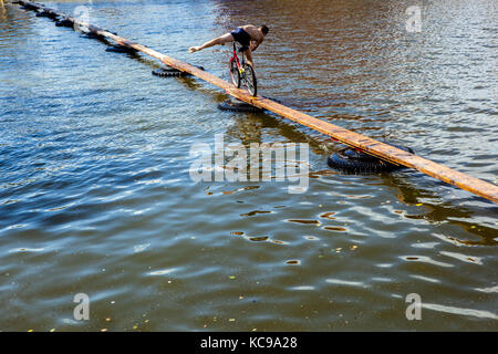 Festival tchèque, sports étranges, CYCLISTE sur une passerelle en bois tente de traverser l'étang, concours toute l'année dans un petit village rural République tchèque Banque D'Images