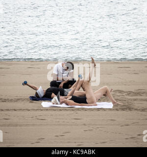 Entraîneur personnel sur la plage de supervision avec deux personnes âgées de levage poids. Banque D'Images