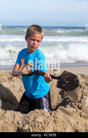 Avon, Outer Banks, Caroline du Nord, USA. Jeune garçon de creuser un trou dans le sable. Banque D'Images