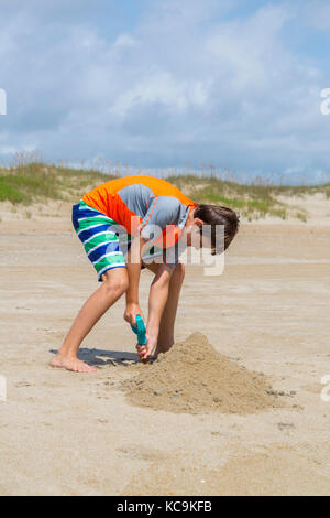 Avon, Outer Banks, Caroline du Nord, USA. Jeune garçon de creuser dans le sable sur la plage. Banque D'Images