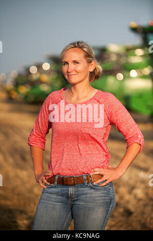 Une jeune PRODUCTRICE SE TROUVE DANS UN CHAMP PRÈS DE MOISSONNEUSES-BATTEUSES JOHN DEERE AVANT LA RÉCOLTE DU BLÉ À LA FERME FAMILIALE PRÈS DE BRECKENRIDGE, DAKOTA DU NORD Banque D'Images