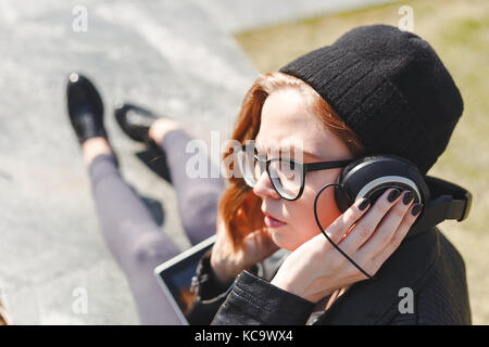 Jolie femme de noir à l'écoute de la musique dans le casque sur la rue et à la voiture. Banque D'Images