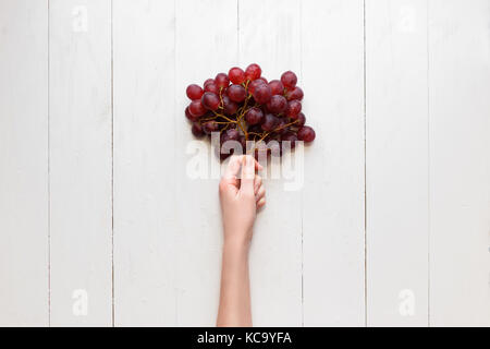 La main de la jeune fille tient à un tas de raisins rouges sur un fond de bois. Vue de dessus. Raisins sont comme des ballons Banque D'Images