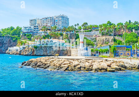 Navigation le long de la jetée dans le vieux port de plaisance avec le petit phare et la rangée de cafés et de magasins sur l'arrière-plan, Antalya, Turquie. Banque D'Images