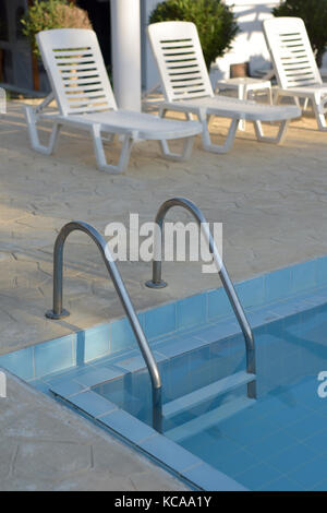 Une échelle en métal ou un ensemble d'étapes d'entrer dans une piscine d'une zone pontés avec transats ou chaises longues. La détente près de la piscine au soleil. Banque D'Images